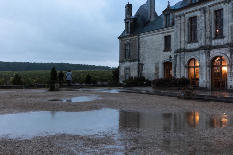 Chateau facade reflected in courtyard puddles near Saint-Emilion after rain at dusk