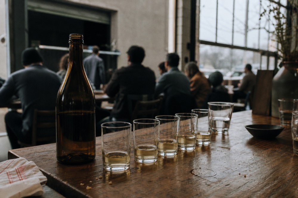 Wine glasses lined up on a wooden tasting table beside an open bottle, no text, no logos, no people