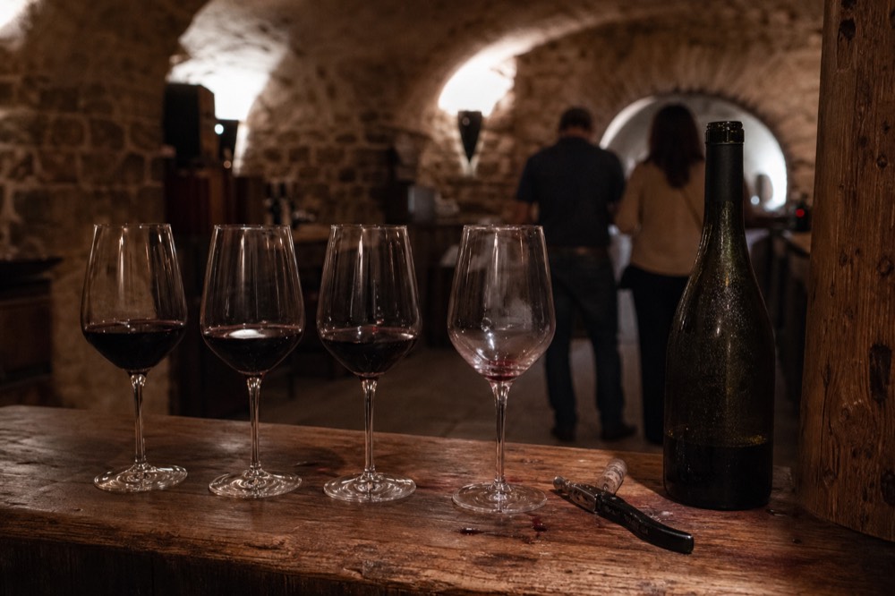 A tasting flight of red Bordeaux wines on a wooden counter in a cellar, no text, no logos, no people